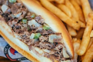 Signature Philly cheesesteak sandwich with ribeye, green peppers, onions, and white American cheese on a hoagie bun with fries