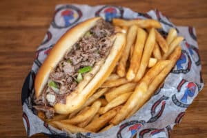 Signature Philly cheesesteak sandwich with ribeye, green peppers, onions, and white American cheese on a hoagie bun with fries