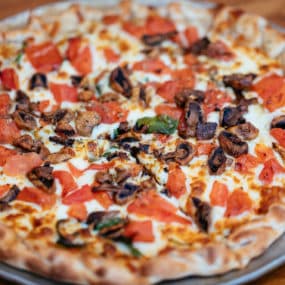Pizza with Spinach, mozzarella, sautéed mushrooms, tomato and oregano sit atop an olive oil base pizza shell.