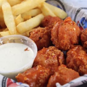 Boneless Wing appetizer consisting of All white meat fried chicken bites tossed in gluten free hot sauce and served with ranch and fries