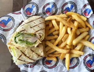 Blackened Chicken romaine lettuce and parmesan cheese inside a white tortilla with fries on The Post Sports Bar & Grill sheet paper